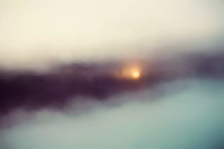 A point of warm light diffusing through pale mist across a distance